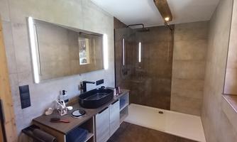 A modern bathroom with a large shower and an elegant sink. The walls are in neutral tones, and there are wooden details.