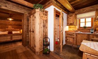 A cozy wooden apartment with rustic furniture and warm lighting. The kitchen is small but well-equipped, and the space exudes an inviting atmosphere.