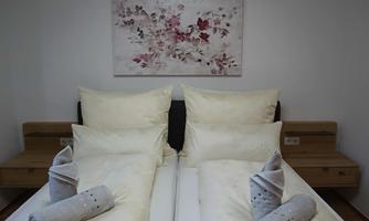 A cozy bedroom with two beds and bright pillows. On the wall hangs a picture with floral motifs.