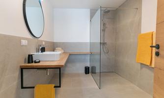 A modern bathroom with a glass shower and a wooden washbasin. The walls are in neutral colors, and a round mirror complements the design.