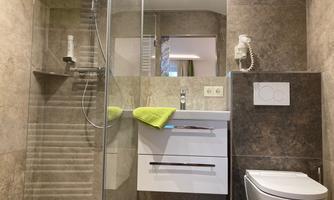 A modern designed shower with a glass wall and a bright shelf. Next to the shower is an elegant sink and a toilet.