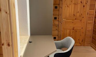 A modern workplace in a wood room with a desk and a comfortable chair. The wall is in neutral colors and the door is made of wood.