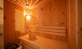 A cozy sauna with wooden walls and benches. A bucket and a ladle are ready to enjoy the sauna experience.