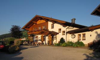 A traditional Alpine building with a wooden facade and a green outdoor area. Outside, tables and chairs are set up, ideal for visitors.