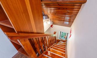 A wooden staircase that leads into a bright room. On the wall are wooden panelings and a window with a view.