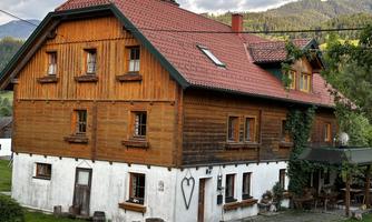 A charming wooden house with a red roof and white walls. It is located in a picturesque landscape with mountains in the background.