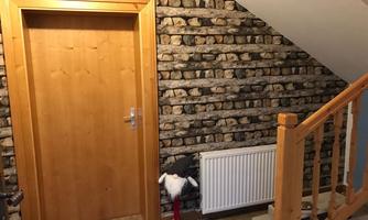 The hallway features a wooden door with a stone-pattern wallpaper. Next to the radiator stands a decorative figure.