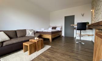 A cozy room with a bed, a couch, and a small table. The room has hardwood floors and a modern atmosphere.