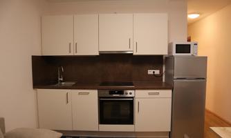 A modern kitchen with white cabinets and a dark countertop. It includes a stove, a refrigerator, and a microwave.