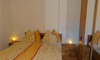 A cozy bedroom with a double bed and colorful cushions. The walls are painted in bright colors, and there are wooden cabinets as well as atmospheric lighting.