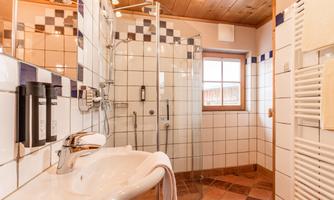 A modern bathroom with a shower and a sink. The walls are tiled and there is a window that lets in natural light.
