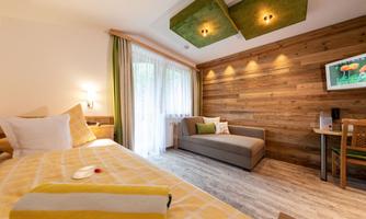 A modern room with wooden paneling and cozy furnishings. There is a bed, a couch, and large windows with curtains.
