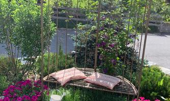 A pretty swing in the garden, surrounded by colorful flowers and green plants. The sky is clear and the atmosphere is peaceful.