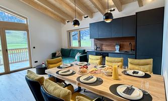 A modern dining area with a long wooden table and colorful chairs. The large windows offer a view of nature outside.