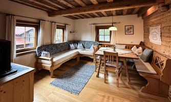 A cozy living space with wooden ceilings and floors. There is a seating area and a dining table, surrounded by large windows.
