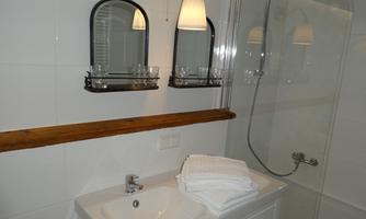 A modern bathroom with a sink, towels, and a shower. The walls are tiled in white and there are two mirrors above the sink.