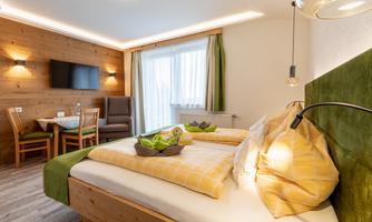 A cozy room with wooden walls, two beds, and a seating area. Large windows provide plenty of daylight and an inviting view outside.