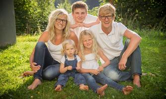A happy family poses outdoors on a green meadow. All members are wearing light clothes and smiling at the camera.
