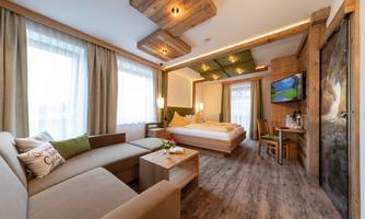 A modern hotel room with a double bed and a cozy seating area. The room design is bright and inviting with wooden details and large windows.