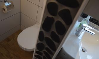 A modern bathroom with a toilet and a sink. The walls are partially tiled, and there is a towel holder.
