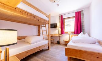 A cozy room with a bunk bed and a single bed. The wooden furnishings create a warm atmosphere.