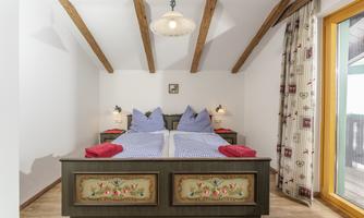 A cozy bedroom with a double bed and traditional wooden elements. Blue pillows and red towels are placed on the bed.