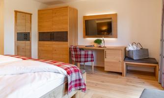A modern bedroom with a wooden bed and a large wardrobe. The room features a desk, a television, and a cozy atmosphere.