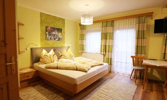A cozy bedroom with a large bed, soft pillows, and a bright, inviting atmosphere. The room features wooden floors and large windows with curtains.