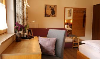 A cozy room with a desk, a couch, and a bed. The decor is modern and inviting, with decorative flowers on the table.