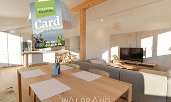 A modern living room with a large dining table and a television. On the table lies the Schladming-Dachstein Card.