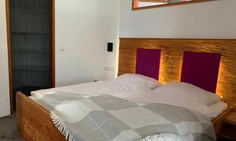 A cozy bedroom with a large double bed and a gray blanket. The walls have wooden details and there is a small window area.