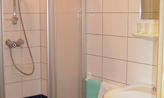 A small bathroom with a shower and a sink. White tiles and a green seating area create a simple, clean look.