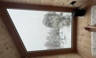 A cozy room with a large window overlooking a snowy landscape. Outside, the trees and ground are covered in fresh, white snow.