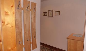 An entrance area with wooden coat hooks on the wall and a small table. Pictures hang on the wall and the floor is covered with a carpet.