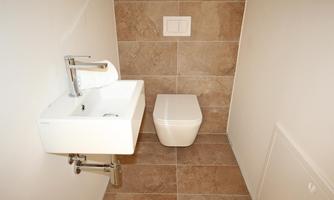 A modern bathroom with a small sink and a toilet. The walls are decorated with light tiles.