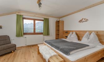 A cozy bedroom with a large bed and wooden interiors. Through the window, you can see the mountains and the room has bright, cheerful colors.
