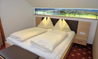 A cozy bedroom with a double bed and two large pillows. A beautiful landscape screen is mounted on the wall behind the bed.