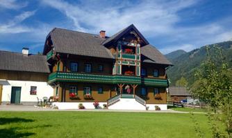A traditional alpine house with colorful flower boxes and detailed wood decorations. The sky is clear and the surroundings are green.
