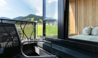 A modern balcony with a view of green hills and mountains in the background. A comfortable seating furniture invites you to relax.