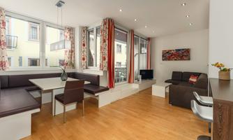 A modern living room with large windows and a cozy dining area. Stylish furniture and bright colors create an inviting atmosphere.