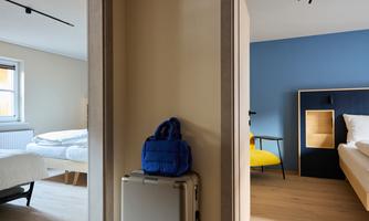 A modern hotel room with two separate sleeping areas. The walls are in soft colors, and a blue backpack is in the middle.