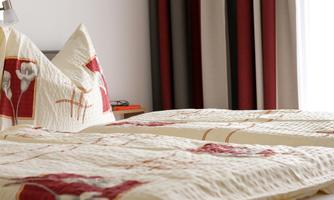 A cozy bedroom with two beds. The bedding has a floral pattern and the curtains are in soft colors.