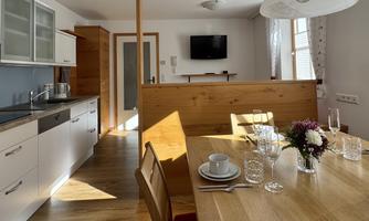 A modern kitchen with a bright dining table and wood-colored accents. The room is well-lit and cheerfully furnished.