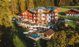 A cozy hotel nestled in nature with colorful balconies. The garden is well-maintained and offers a pool as well as relaxed seating options.