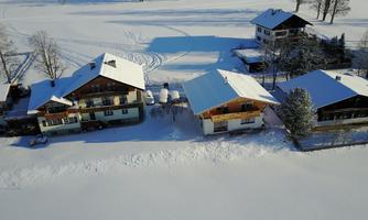 A quiet winter landscape with snow-covered houses. The snow blankets the ground and there are some trees visible in the background.