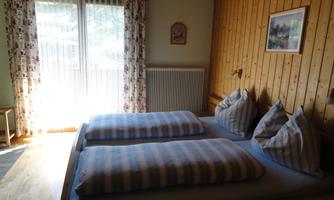 A cozy bedroom with a double bed and striped bedspreads. Large windows with draped curtains let in plenty of light.