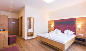 A bright and modern bedroom with a double bed and wooden-paneled walls. The room includes a mirror, a small seating area, and a cozy atmosphere.