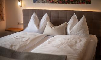 A cozy double bed with white pillows and a gray blanket. The tranquil atmosphere is enhanced by gentle light and a bright wall design.