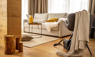 A cozy living room with a bright sofa, a table, and a rug. Next to the sofa, blankets and pillows lie on the floor.