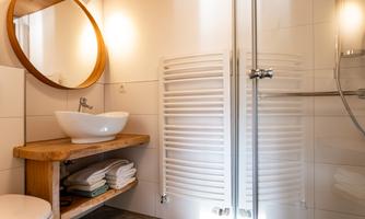 A modern bathroom with an elegant shower and a round mirror.  

Wooden shelves with towels and pleasant lighting create an inviting atmosphere.